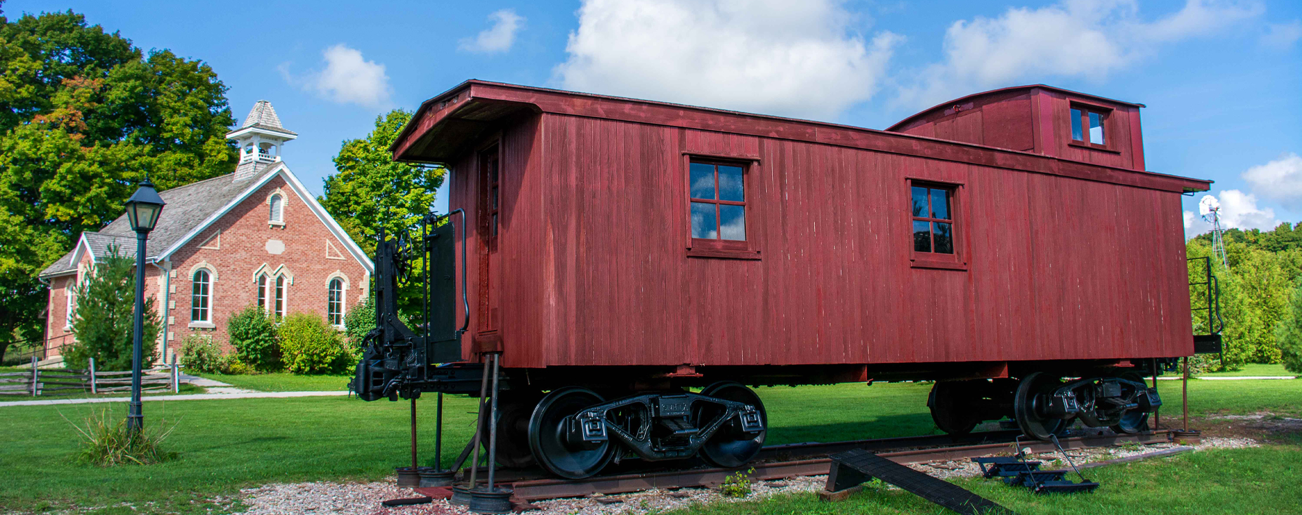 A red caboose stands above green grass on a dark cloudy day.