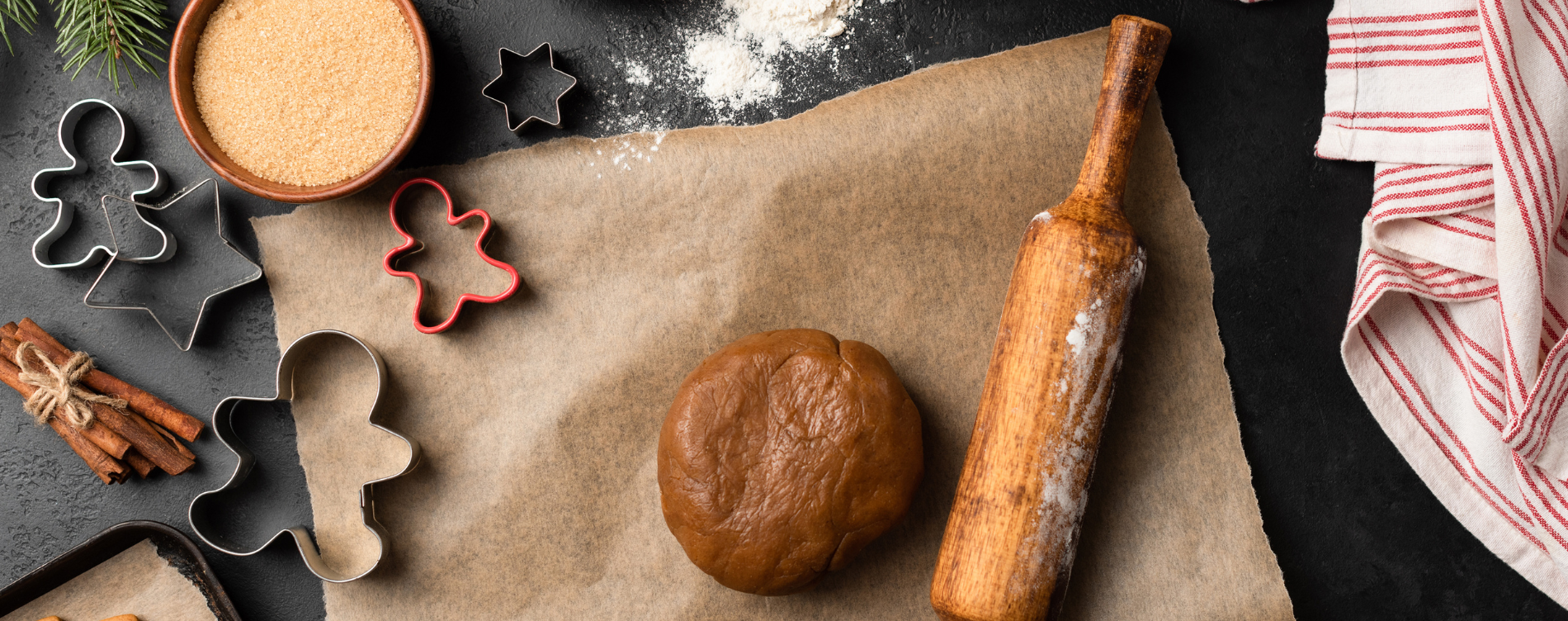 Spiced cookie dough balled up beside a wooden rolling pin and cookie cutters in the shape of a five point star and people.