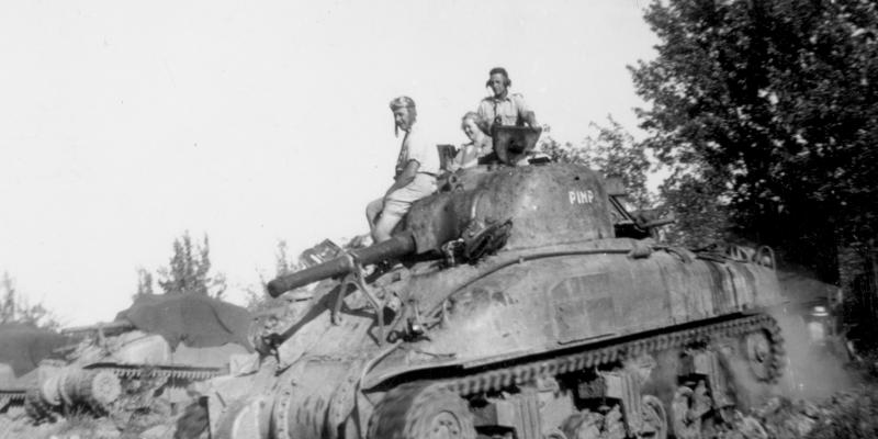 Black and white image of three people riding a Second World War army tank.