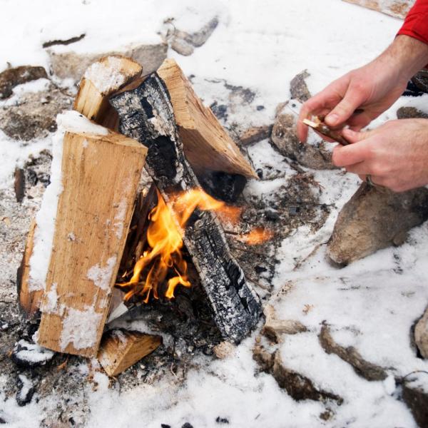 Two hands tending to burning campfire in winter.