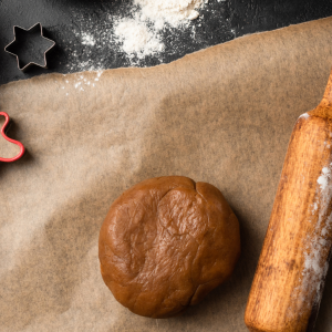 Spiced cookie dough balled up beside a wooden rolling pin and cookie cutters in the shape of a five point star and people.